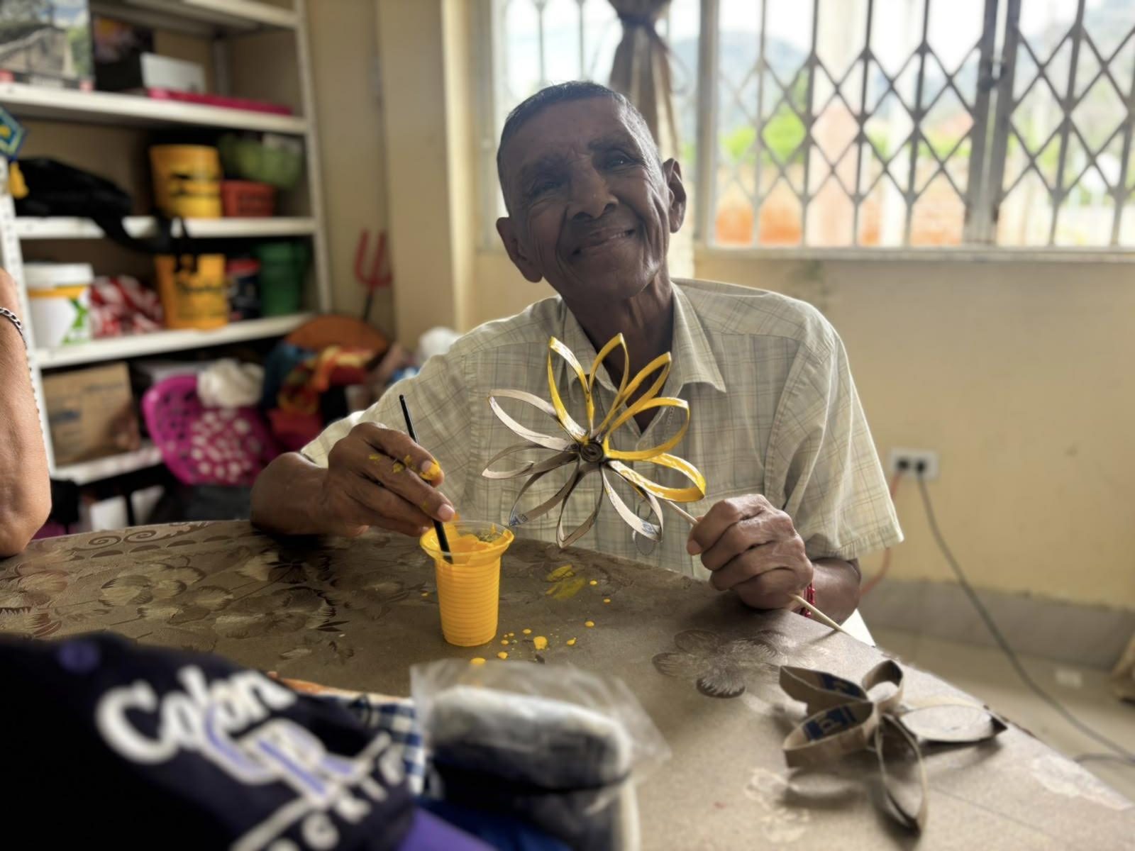Un adulto mayor pinta una flor de papel